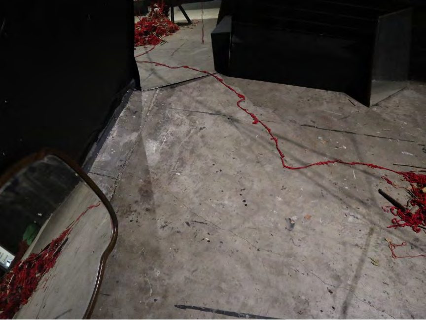 Red yarn crossing a concrete floor in a dim gallery