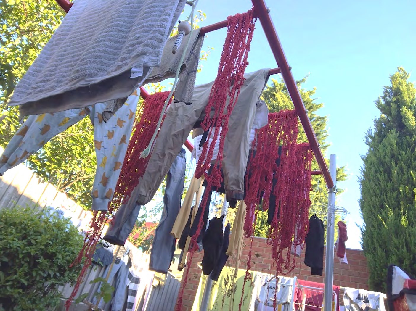 Lengths of red hemp yarn hanging from a clothesline among laundry