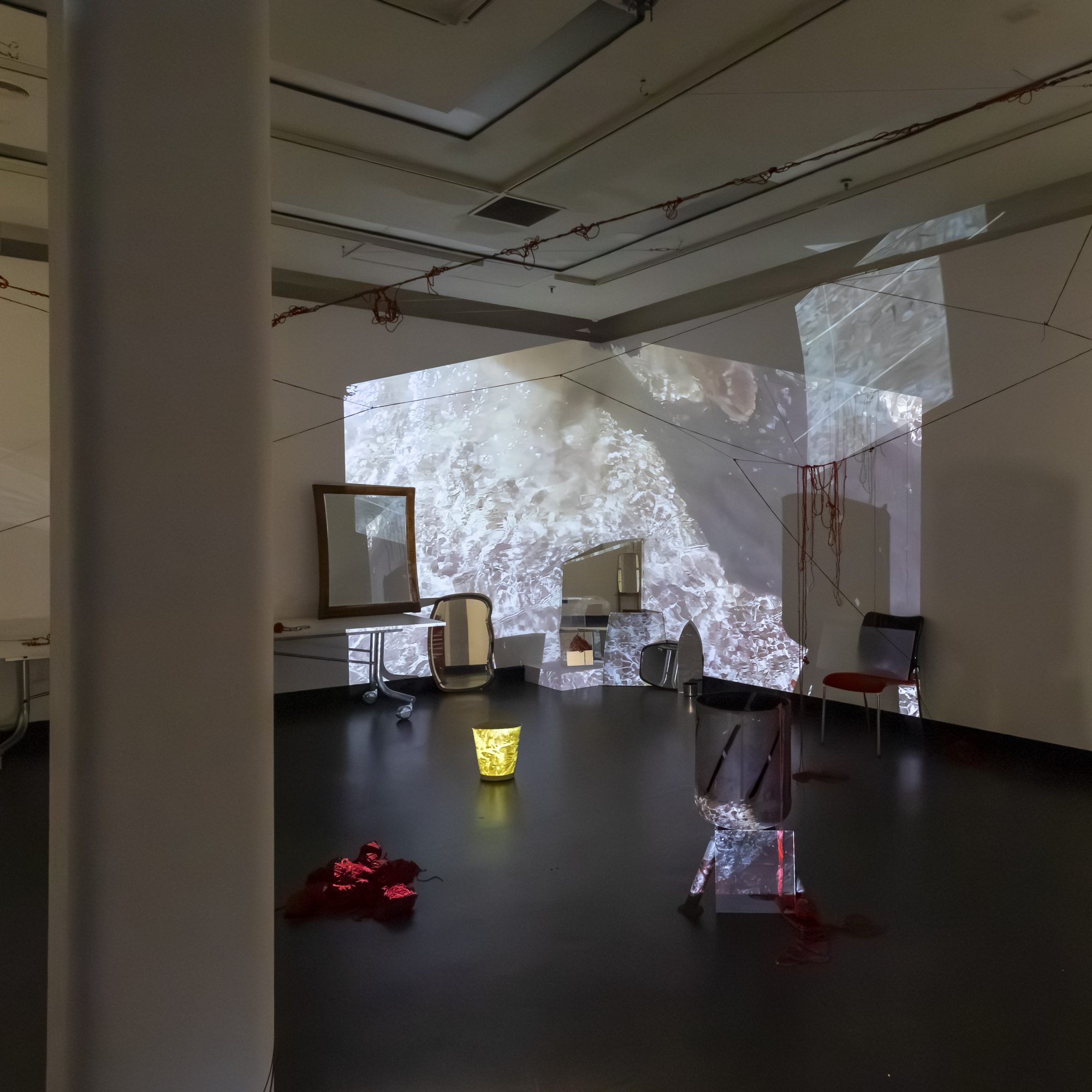 A projection of rippling water behind a mirror, chairs and small lit objects