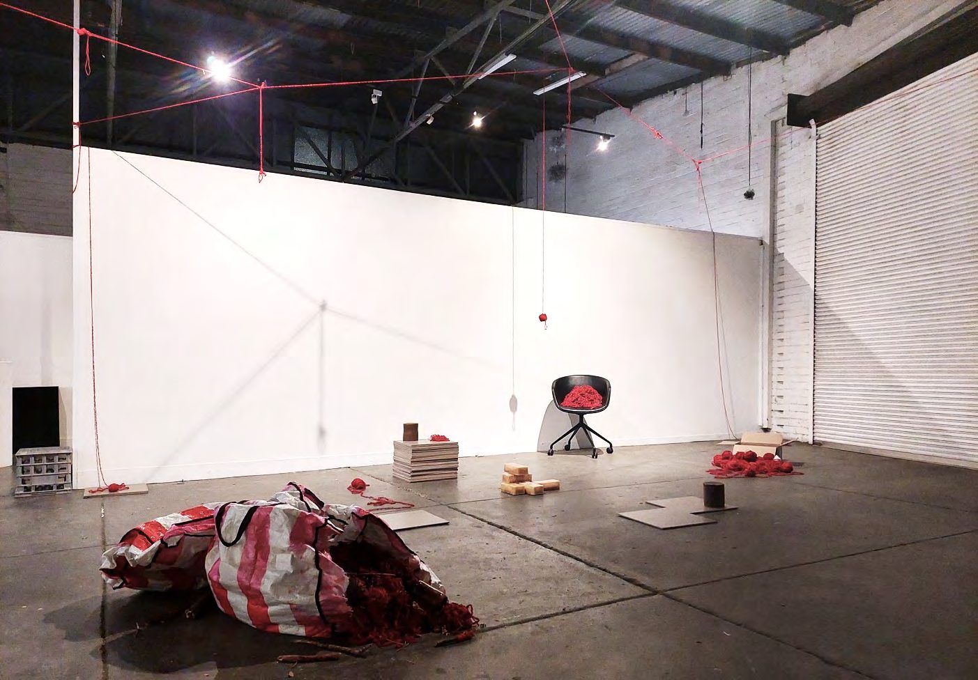 A gallery with red yarn lines, a striped bag of yarn on the floor, and a desk and chair