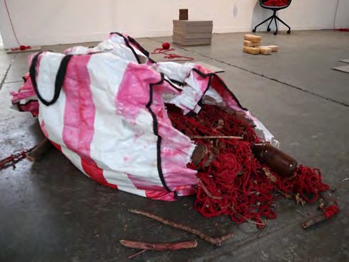 A striped plastic bag spilling red yarn and found materials on a concrete floor