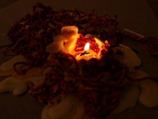A beeswax candle burning within a nest of red yarn