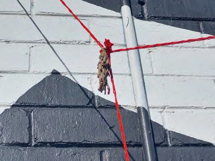 A knot of red yarn tied to a pole against a painted brick wall