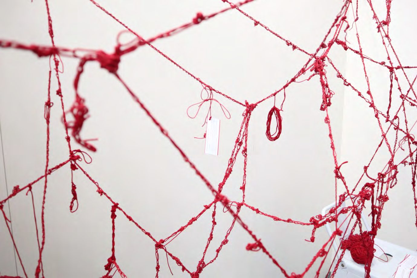 Red yarn knotted into a dense hanging web with small tags